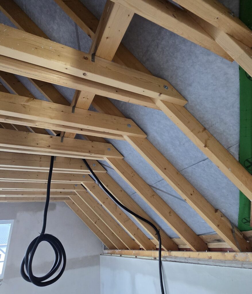 Dachboden mit sichtbaren Holzbalken und Kabeln.